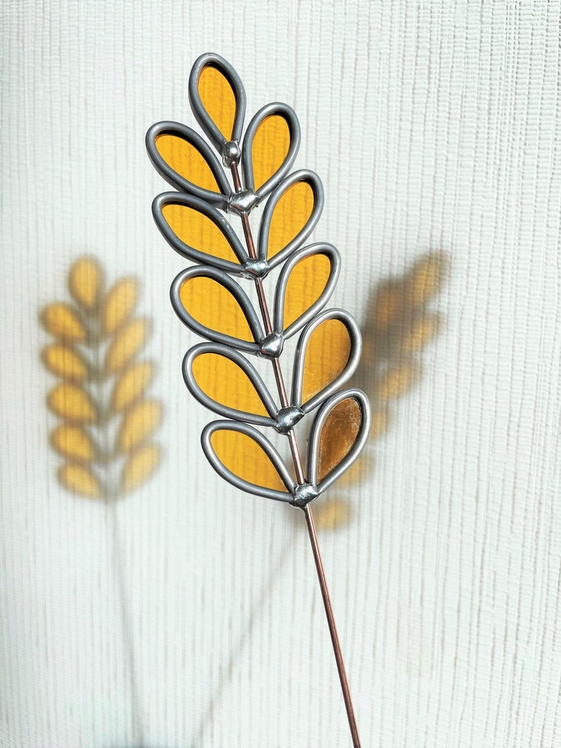 May include: A stained glass floral stem with yellow glass leaves and a silver wire frame. The stem is attached to a copper wire.