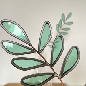 May include: A decorative metal branch with green glass leaves. The branch is made of copper wire and the leaves are made of stained glass.