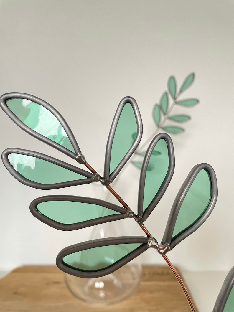 May include: A decorative metal branch with green glass leaves. The branch is made of copper wire and the leaves are made of stained glass.
