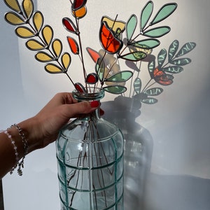 May include: A bouquet of stained glass flowers in shades of red, orange, yellow, and green, arranged in a clear glass vase with a grid pattern.