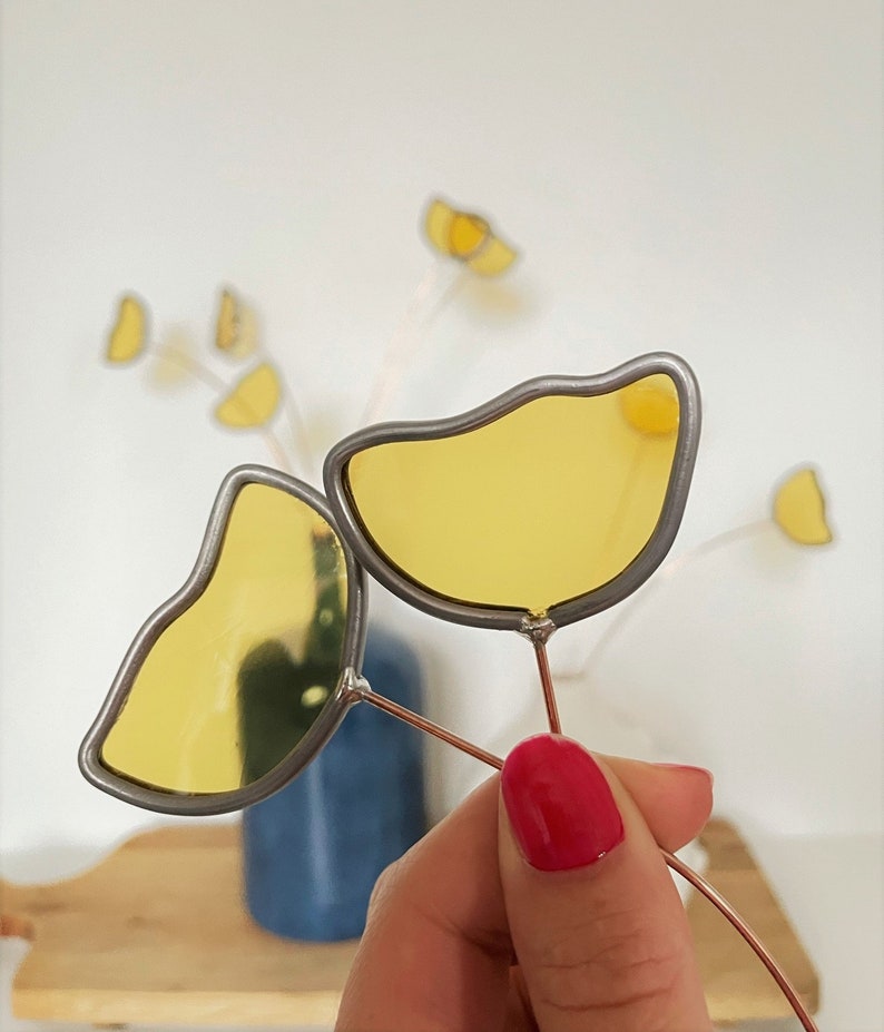 May include: Two yellow stained glass flowers with silver wire stems. The flowers are in the shape of a teardrop and a half-circle.