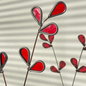 May include: A stained glass art piece featuring a red leaf design with a silver wire frame. The leaves are shaped like teardrops and are arranged in a cluster.