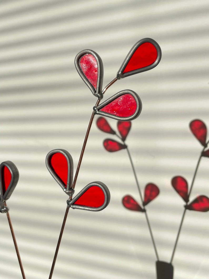 May include: A stained glass art piece featuring a red leaf design with a silver wire frame. The leaves are shaped like teardrops and are arranged in a cluster.