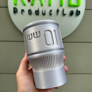 May include: A cylindrical, silver-colored product with the text "ww 01" engraved on its side. The product has a ribbed lower section and is held in a hand. The background features the text "RATIO ProductLab".
