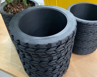 May include: Three black cylindrical planters with a tire tread pattern. The planters are made of a textured material and are empty.