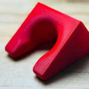 May include: A vibrant red, U-shaped object with a smooth, curved interior and angled exterior sides. The object appears to be made of a solid material, possibly plastic or resin. The design is modern and geometric.
