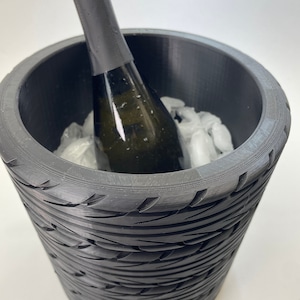 Może przedstawiać: Czarny chłodziarka do wina z fakturą opony, zawierająca butelkę wina i lód.