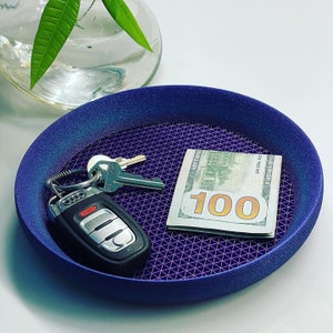 May include: A purple tray with a geometric pattern and a $100 bill, a car key, and a key on top.