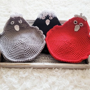 Puede incluir: Tres salvamanteles de ganchillo con forma de pájaro en una bandeja de madera. Los salvamanteles son de color gris, negro y rojo. Cada salvamanteles tiene una cresta y rasgos faciales de ganchillo blancos o grises. Los salvamanteles son circulares con un borde festoneado.