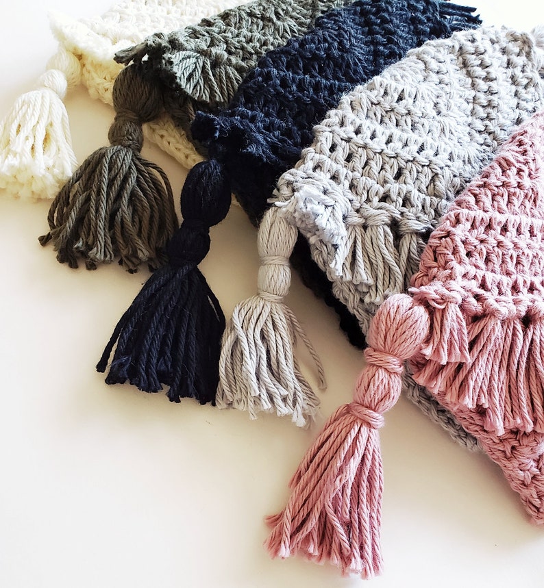 Puede incluir: Cinco gorros de crochet con borlas en varios colores, incluyendo blanco, verde, negro, gris y rosa.