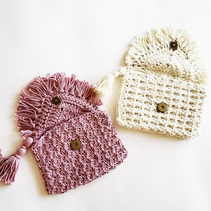 Puede incluir: Dos bolsos de crochet con detalles de flecos. Un bolso es rosa y el otro es blanco.