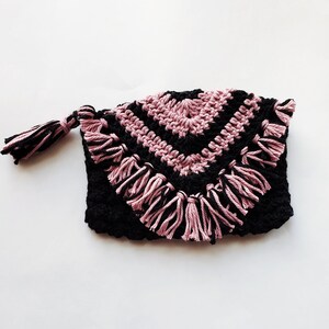 Puede incluir: Una bolsa de crochet negra y rosa con un borla. La bolsa tiene un patr&oacute;n geom&eacute;trico y un borde de flecos.