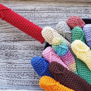 Puede incluir: Una colección de agarraderas de olla de ganchillo de colores, en una variedad de colores, incluyendo rojo, rosa, azul, verde, amarillo y blanco. Las agarraderas de olla están dispuestas en un círculo, con la agarradera de olla roja en la parte superior.