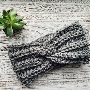 May include: A gray crocheted headband with a twisted design. The headband is made of a soft, textured yarn.