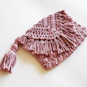 May include: A pink crocheted blanket with a fringe border and a tassel. The blanket is made with a soft, textured yarn.