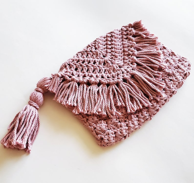 Puede incluir: Una manta de crochet rosa con un borde de flecos y un borla. La manta est&aacute; hecha con un hilo suave y texturizado.