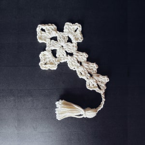 May include: A white crocheted cross bookmark with a tassel. The cross is made of a delicate, intricate pattern.