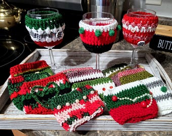Può includere: Un set di sette copri bicchieri da vino all'uncinetto in vari motivi natalizi, tra cui rosso, verde, bianco e nero. I copri bicchieri presentano una varietà di decorazioni, come bottoni, perline e cuori di lana.