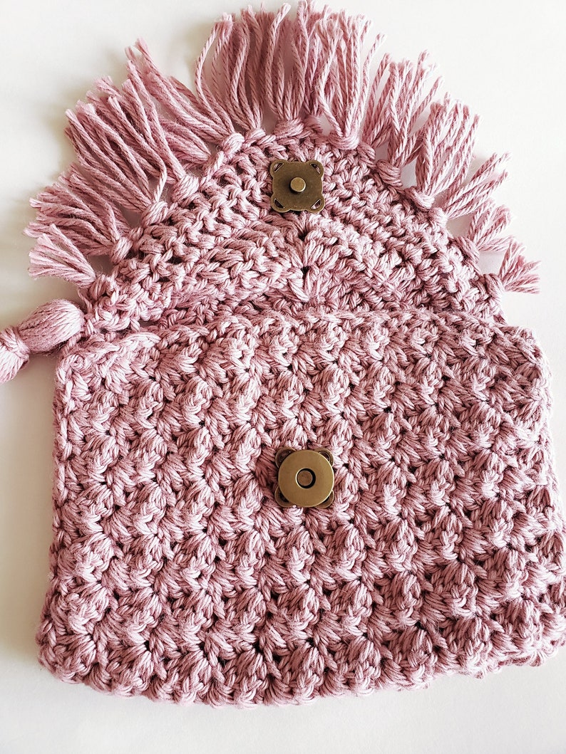 Puede incluir: Una bolsa de crochet rosa con un dise&ntilde;o texturizado y detalles de flecos. La bolsa tiene dos cierres magn&eacute;ticos de lat&oacute;n.