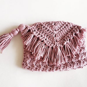 Puede incluir: Una bolsa de crochet rosa con un borla. La bolsa tiene un borde festoneado y est&aacute; decorada con flecos.