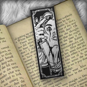 May include: Black and white bookmark featuring a line drawing of a woman with a tear running down her cheek. The woman is holding a knife to her neck. The bookmark has a silver foil finish and the text "remarkable" is visible in the background.