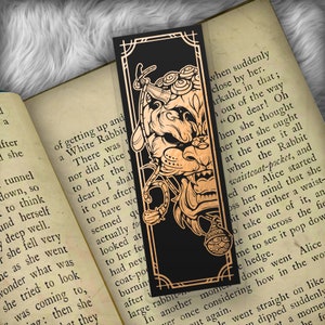 May include: A black bookmark with a gold design of a rabbit with a pocket watch and a key. The bookmark has the text "when suddenly close by her. arkable in that; out of the way "Oh dear! Oh hen she thought her that she ought at the time it all when the Rabbit waistcoat-pocket, and ed on, Alice started oss her mind that she bit with either a waist- o take out of it, an he ran across the fie me to see it pop dow e hedge. down went Alice ver once considering how in the wor t again. le went straight on like dipped suddenly ot a momen he fo"