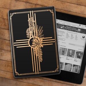 May include: A black and gold e-reader cover with a stylized design of a cross with a floral pattern. The cover is on a wooden surface.