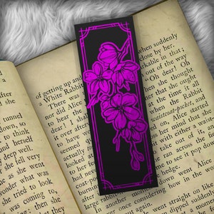 May include: A black bookmark with a pink floral design. The bookmark features a quote from Alice in Wonderland: "Oh dear! Oh when she thought that she ought at the time it all when the Rabbit waistcoat-pocket, and ed on, Alice started oss her mind that she bit with either a waist- o take out of it, an he ran across the fie me to see it pop dow e hedge."