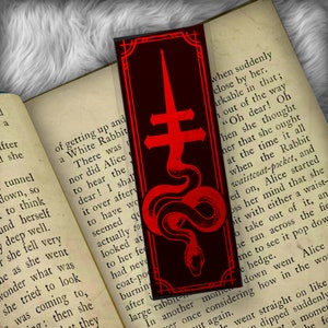 May include: A black bookmark with a red snake wrapped around a red cross. The bookmark has a black border and a red background.