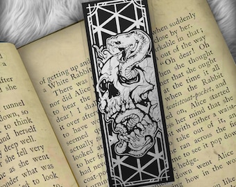 May include: Black and white bookmark featuring a skull with a snake wrapped around it. The bookmark has a geometric pattern in the background.