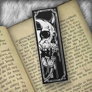 May include: Black and white bookmark featuring a skull with a dripping black substance. The bookmark has a white border and a silver inscription that reads "F".