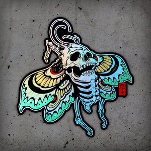 May include: A colorful sticker featuring a skeletal butterfly with a skull head. The butterfly has iridescent wings with black outlines and red accents. The skull has a toothy grin and is outlined in black.