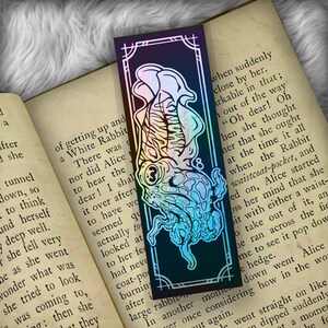 May include: A holographic bookmark featuring a colorful illustration of a squid with tentacles. The bookmark has a black background with a white border. The text "when suddenly close by her. arkable in that; out of the way "Oh dear! Oh hen she thought her that she ought at the time it all when the Rabbit waistcoat-pocket, and ed on, Alice started oss her mind that she bit with either a waist- o take out of it, an he ran across the fie me to see it pop dow e hedge. down went Alice how in the wo le went straight on like dipped suddenly ot a momen he fo" is visible on the bookmark.