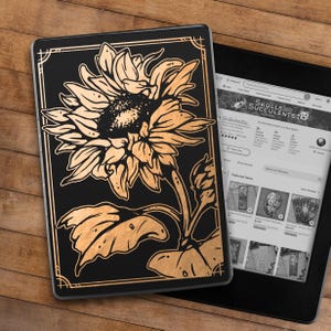 May include: A black and gold e-reader case with a sunflower design. The case has a gold border and a black background. The sunflower is in the center of the case and is facing to the right. The sunflower is made of gold foil and has a detailed design.