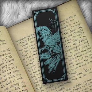 May include: A black bookmark with a teal blue illustration of a bird with a chain around its neck. The bookmark has a decorative border and the text "remarkable" is visible on the right side of the bookmark.
