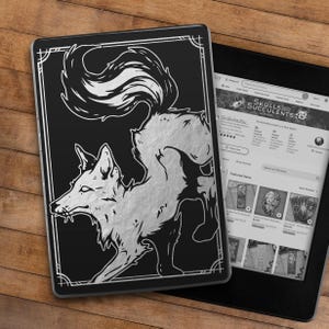 May include: A black and silver e-reader case with a graphic of a stylized fox with a white stripe on its tail. The fox is facing left and has a menacing expression.