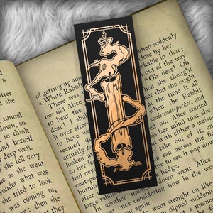 May include: A black bookmark with a gold illustration of a candle with smoke rising from the wick. The bookmark has a decorative border and the text "when suddenly close by her. arkable in that; out of the way "Oh dear! Oh hen she thought her that she ought at the time it all when the Rabbit waistcoat-pocket, and ed on, Alice started oss her mind that she bit with either a waist- o take out of it, an he ran across the fie me to see it pop dow e hedge. down went Alice ver once considering how in the wor t again. le went straight on like dipped suddenly ot a momen he fo"