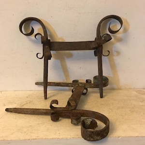 May include: A pair of antique iron candle holders with ornate scrollwork. The holders are rusted and have a rustic appearance.