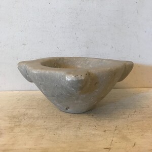 May include: A white marble mortar with a wide, shallow bowl and a slightly flared rim. The mortar has a rough, textured surface and is slightly chipped in places.