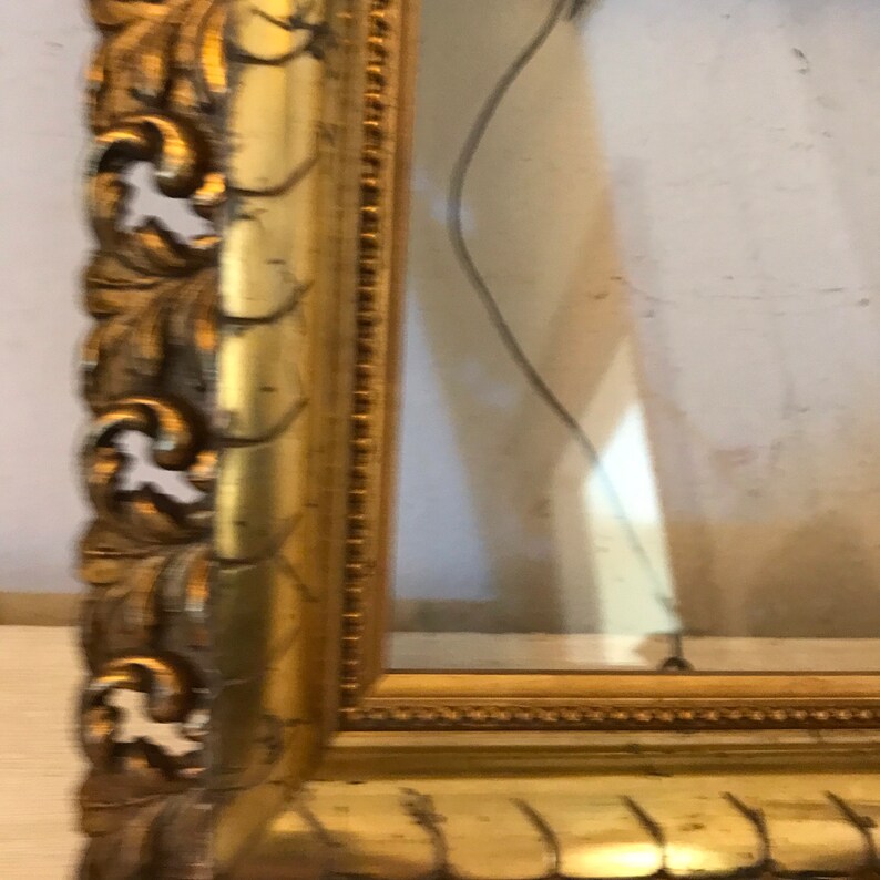 K&ouml;nnte beinhalten: Ein verzierter Bilderrahmen in Gold mit einem detaillierten, geschnitzten Design. Der Rahmen ist leicht besch&auml;digt, einige der goldenen Farbe sind abgeplatzt.