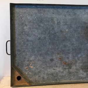 May include: A large, rectangular, galvanized metal tray with a handle on the side. The tray has a drain hole in one corner and shows signs of wear and rust.