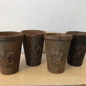May include: Four vintage cast iron flower pots with a fleur-de-lis design. The pots are in various shades of brown and black.