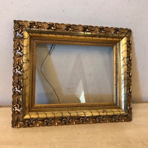 K&ouml;nnte beinhalten: Ein verzierter Bilderrahmen in Gold mit einem dekorativen, geschnitzten Design. Der Rahmen ist leer und bereit, ein Foto oder ein Kunstwerk zu pr&auml;sentieren.