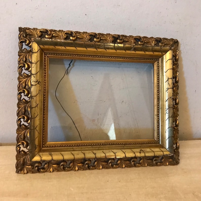 K&ouml;nnte beinhalten: Ein verzierter Bilderrahmen in Gold mit einem dekorativen, geschnitzten Design. Der Rahmen ist leer und bereit, ein Foto oder ein Kunstwerk zu pr&auml;sentieren.