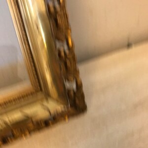 K&ouml;nnte beinhalten: Nahaufnahme eines goldenen Bilderrahmens mit verzierten Details. Der Rahmen ist aus Holz und hat eine patinierte Oberfl&auml;che.