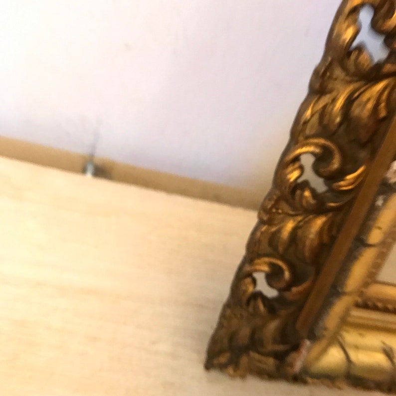 K&ouml;nnte beinhalten: Ein verzierter Bilderrahmen in Gold mit einem detaillierten, komplizierten Design. Der Rahmen ist aus Metall und hat eine leicht gealterte Optik.