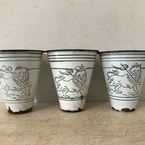 May include: Three white enamelware cups with black lion designs. Each cup has a black rim and a black lion design with a crown on its head.