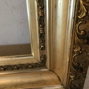May include: A close-up of a gold picture frame with ornate details. The frame is slightly distressed, giving it a vintage look.