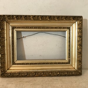 May include: A gold-colored ornate picture frame with a decorative border. The frame is empty and ready to display a picture or artwork.