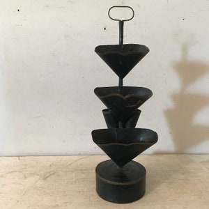 May include: A black metal tiered stand with three round, scalloped trays. The stand has a handle at the top and a round base.